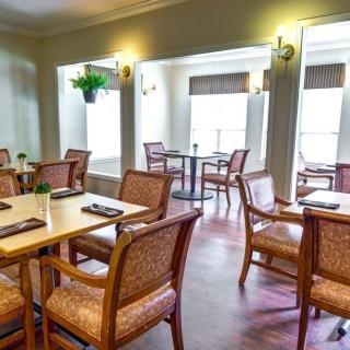 A cozy dining area featuring wooden chairs and tables with plenty of natural light streaming in through large windows.