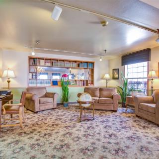 A cozy living room with comfortable sofas and armchairs, a patterned carpet, and a well-stocked bookshelf.