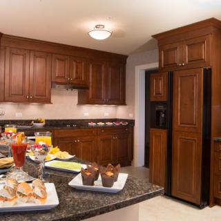 A modern kitchen with wooden cabinets, dark countertops, and a variety of food items displayed.