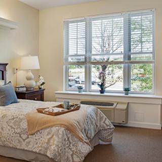 A cozy bedroom with a neatly made bed, illuminated by natural light from a large window.