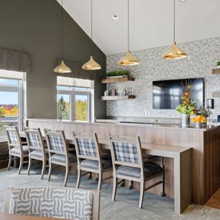 A modern dining area with a long table, plaid chairs, and stylish pendant lights in a contemporary setting.
