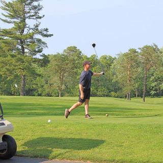 A golfer swinging on a lush green golf course under a clear blue sky.