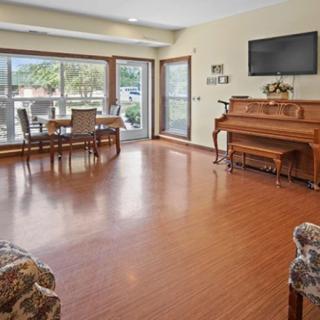 A spacious living room with a piano, dining table, and large windows allowing natural light to fill the space.