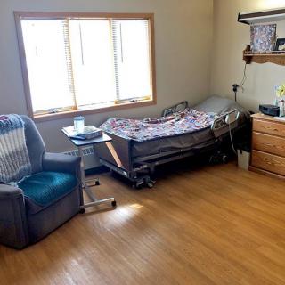 A cozy bedroom with a hospital bed, comfortable chair, and natural light from the window.