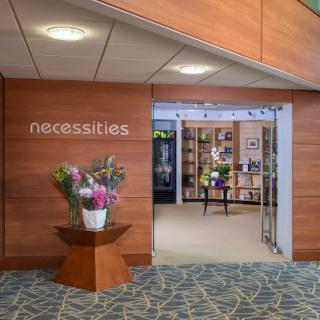 A welcoming entrance to a store named 'necessities', adorned with fresh flowers and modern interior design.