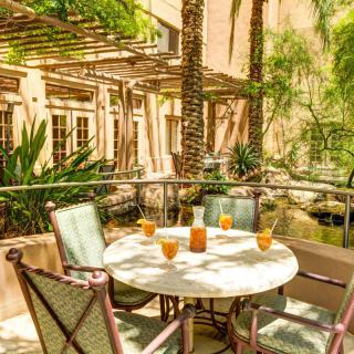 A sunny patio with a round table and chairs, surrounded by lush tropical plants.