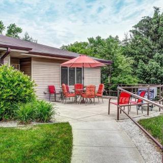 A cozy backyard patio with red chairs and an umbrella next to a house, surrounded by lush greenery.