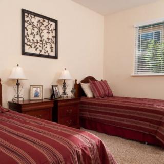 A cozy bedroom featuring twin beds with red striped bedding, nightstands adorned with lamps and personal photos, and a window with blinds letting in natural light.