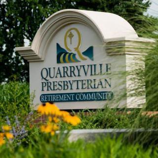 Sign for Quarryville Presbyterian Retirement Community surrounded by flowers and greenery.