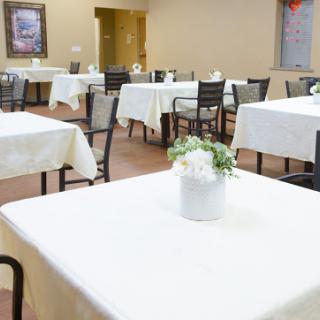 A neatly arranged dining area with white tablecloths and floral centerpieces, showcasing a serene restaurant atmosphere.