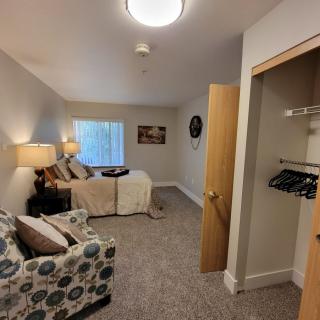 A cozy bedroom with a bed, sofa, lamps, and a small closet.
