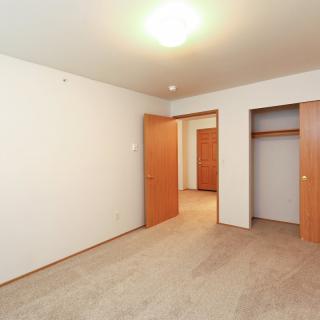 An empty room with a carpeted floor, a closet, and wooden doors.