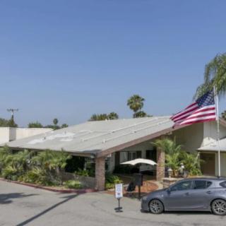 A residential building with an American flag and a car parked in the driveway, surrounded by palm trees under a clear blue sky.