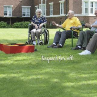 A group of seniors enjoying a sunny day outdoors, sitting on the lawn and engaging in conversation.