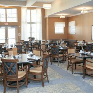 A modern dining room with neatly arranged tables and chairs, featuring large windows and neutral tones.