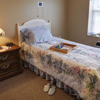 A cozy bedroom with a single bed, a floral bedspread, and a wooden nightstand beside a lamp.