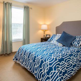 A cozy bedroom with a patterned bedspread, soft lighting from a lamp, and a window with curtains.