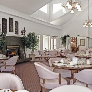 An elegant dining room with skylights, featuring neatly arranged tables and chairs, decorated with plants and a cozy fireplace.