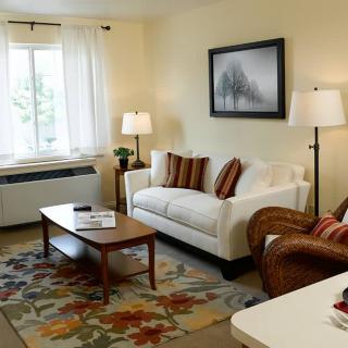 A cozy living room with a sofa, armchair, and coffee table, complemented by a carpet and decorative artwork.