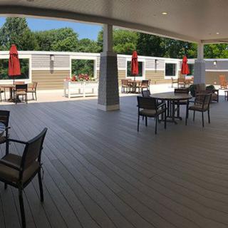 A spacious outdoor patio area with tables and chairs, sheltered under a covered section and featuring red umbrellas.
