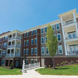 A modern apartment building featuring balconies and a well-maintained landscape under a clear blue sky.