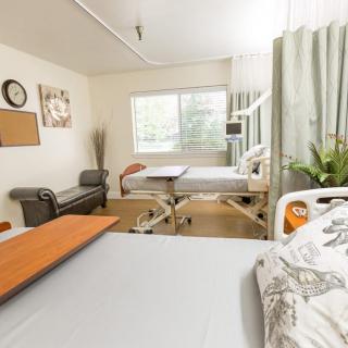 A clean and well-organized hospital room featuring a bed, furniture, and large window for natural light.