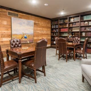 A cozy reading room with leather chairs, wooden tables, and bookshelves filled with books.