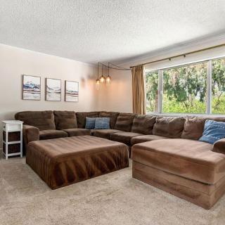 A cozy living room featuring a large brown sectional sofa and a matching ottoman, with natural light streaming in through a sizable window.