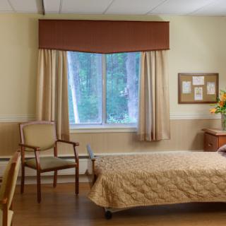 A serene hospital room featuring a bed, chair, and a view of nature through the window.