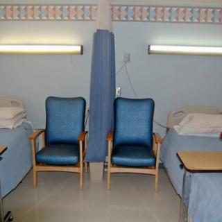 A hospital ward with two beds, chairs, and a divider curtain.