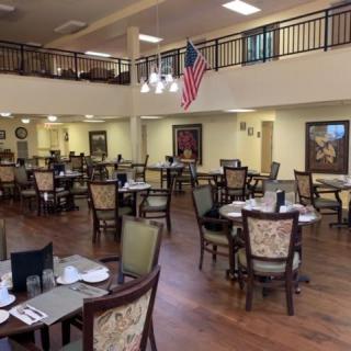 Spacious dining area with neatly arranged tables and chairs, featuring a large American flag and elegant chandeliers.