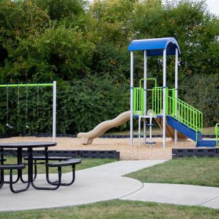 A small playground featuring a slide, swing set, and picnic table in an outdoor park setting.