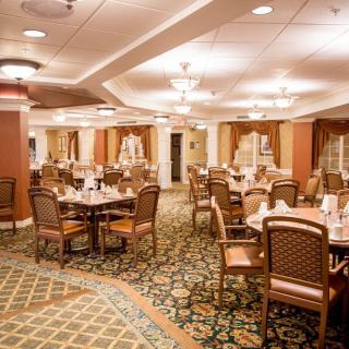 An elegant dining room with neatly arranged tables and chairs, featuring warm lighting and a patterned carpet.