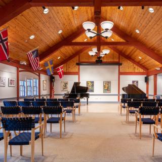 A cozy concert hall with two grand pianos, chairs arranged for an audience, and international flags adorning the walls.