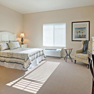 A cozy bedroom with a neatly made bed, armchair, and soft natural lighting from the window.