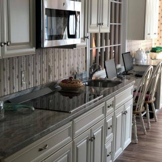 A modern kitchen with sleek countertops, featuring a microwave, laptops on the counter, and a cupcake stand.