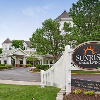 A picturesque view of a senior living facility, surrounded by greenery and featuring a welcoming entrance sign.