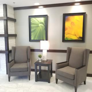 A cozy seating area in a modern interior space featuring two armchairs, a small table with a lamp, and decorative wall art.