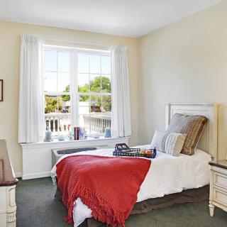 A cozy bedroom featuring a single bed with a red blanket near a large window.