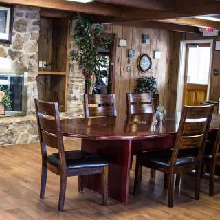 A cozy dining area with a wooden table, chairs, and a stone fireplace, featuring rustic decor and indoor plants.