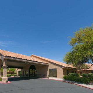 A single-story building with a tiled roof and arched entrance, surrounded by trees and an empty parking lot under a clear blue sky.