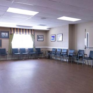 An empty waiting room with chairs lined against the walls and natural light coming through a window.
