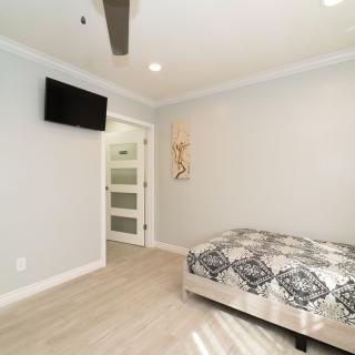 A modern minimalist bedroom with a television, elegant bedding, and wooden flooring.