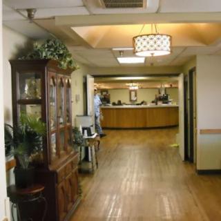 A hallway in a building with wooden floors, decorative furniture, and plants leading to a reception area.