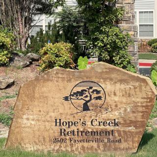 A stone sign for Hope's Creek Retirement community surrounded by landscaping.