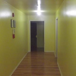A well-lit hallway with yellow walls and a wooden floor leading to a doorway.