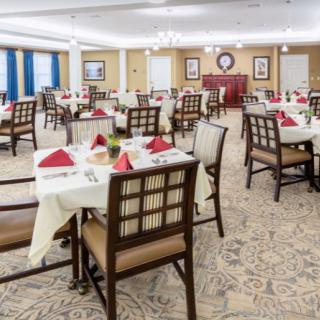 An elegant dining room with neatly arranged tables and chairs, featuring red napkins and tasteful decor.