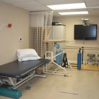 A rehabilitation room equipped with exercise equipment and a treatment bed.
