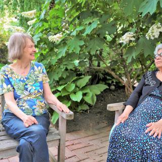 Two women sitting on benches and having a conversation in a garden.