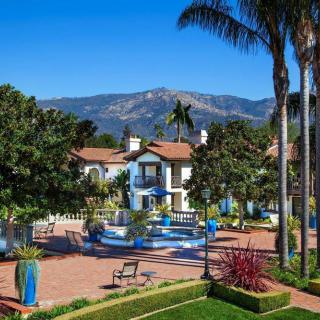 A luxurious resort with Mediterranean-style architecture surrounded by lush landscaping and palm trees, set against a backdrop of mountains.